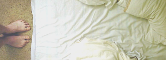 A person standing facing an unmade bed